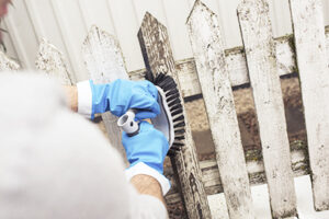 Person borstar staket innan målning utomhus