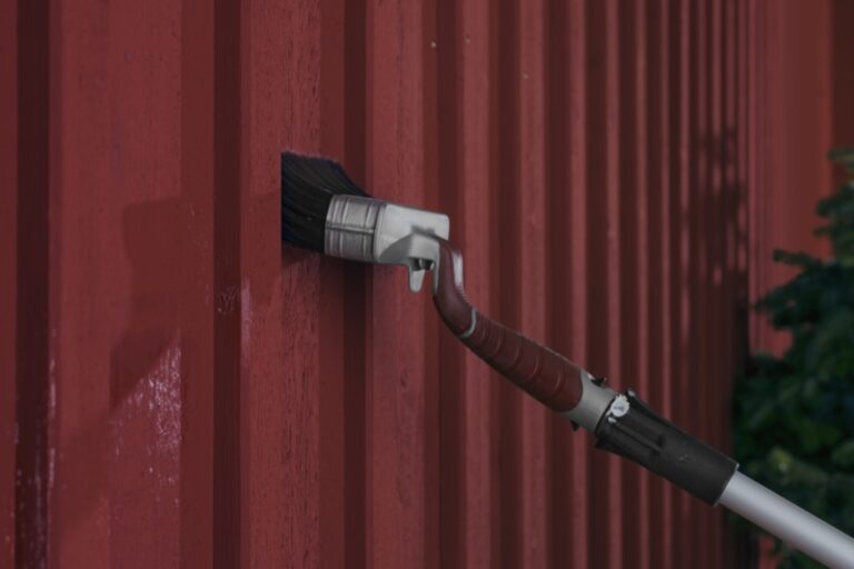 Anza rödfärgspensel med förlängningsskaft målar med falurödfärg på husfasad