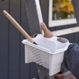 Kädessä pidettävä värikaukalo, joka lepää tikkaita kiipeilevän käden varassa.